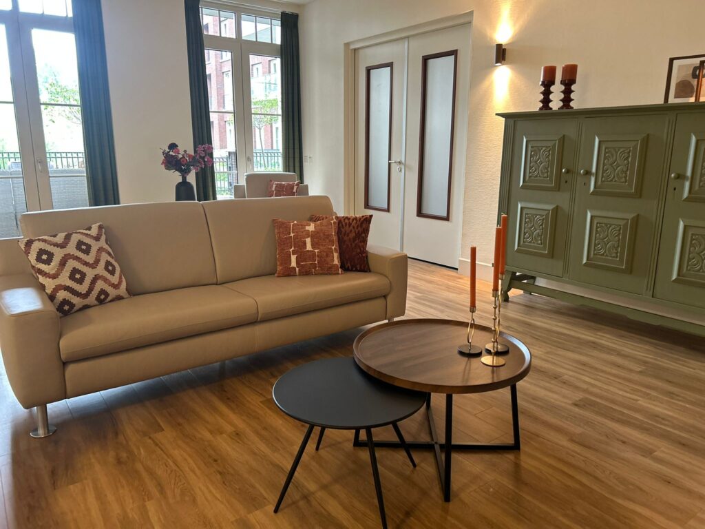 Foto van ingerichte huiskamer met beige bank, tafeltje en groene kast